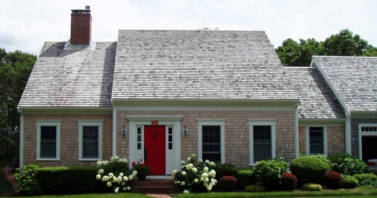 Cape Cod home with a red front door and landscaped yard.